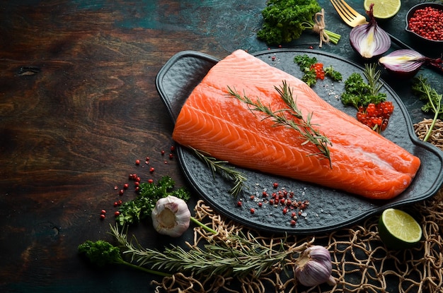 Filetto di salmone crudo con rosmarino su una lastra di pietra nera su sfondo scuro Piatto lay