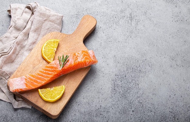 Filetto di salmone crudo con spicchi di limone e rosmarino su tagliere di legno