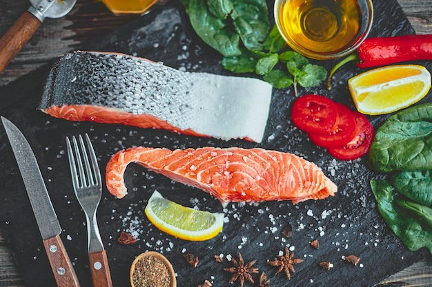 Filetto di salmone crudo e ingredienti per cucinare su un tavolo scuro