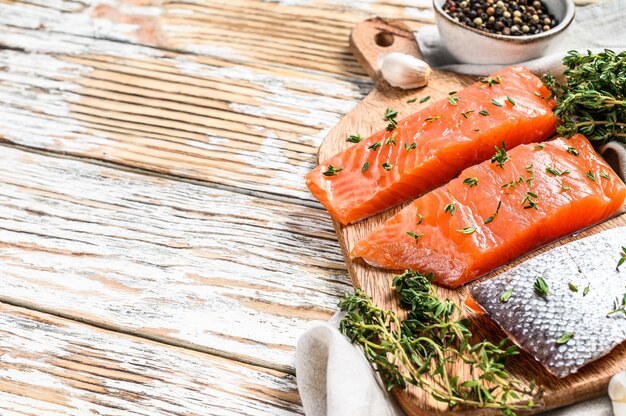 Filetto di salmone dell'Atlantico fresco su un tagliere. Fondo in legno bianco. Vista dall'alto. Copia spazio.