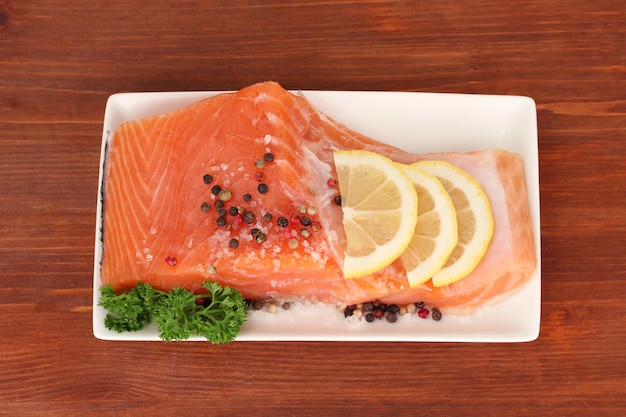 Filetto di salmone fresco con prodotti di erboristeria e fettine di limone sulla piastra su fondo di legno