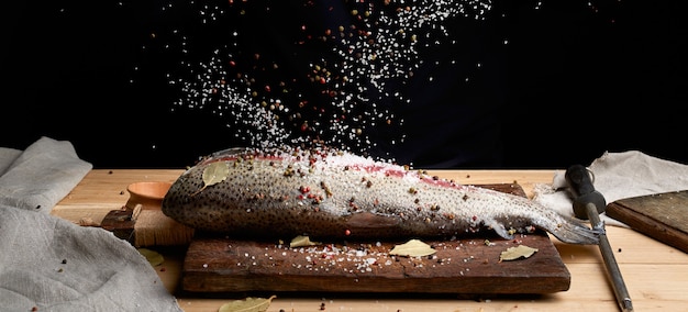 Filetto di salmone senza testa su una tavola di legno cosparsa di grande sale bianco e pepe