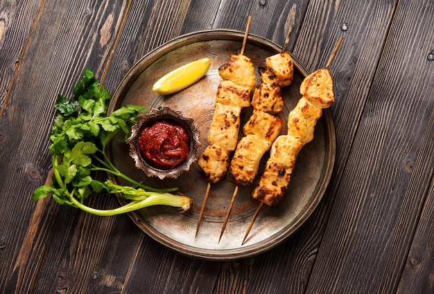 Filetto di shish kebab di tacchino su spiedini di bambù su una piastra di metallo su un tavolo in legno vista dall'alto