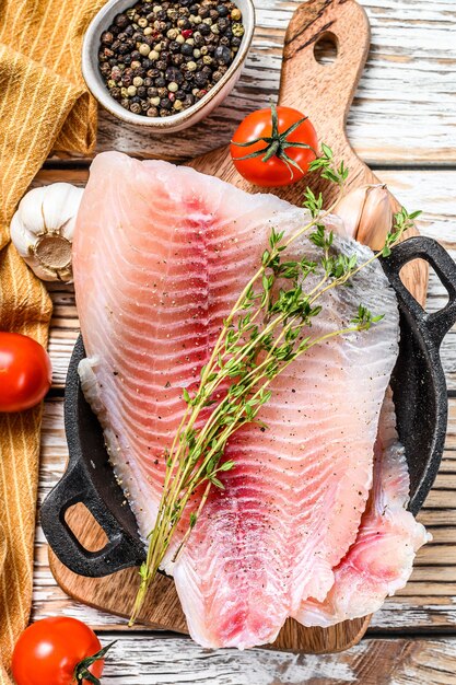 Filetto di telapia fresco ia una padella. Fondo in legno bianco. Vista dall'alto.