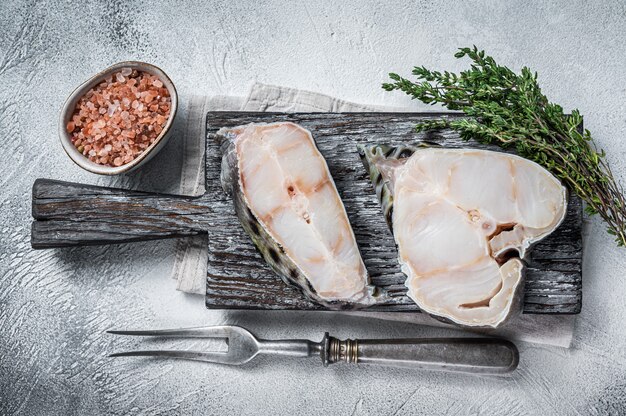 Filetto di wolffish crudo bistecca di pesce sul tagliere di legno. Tavolo bianco. Vista dall'alto.