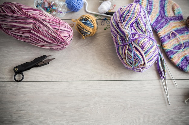 Fili colorati ferri da maglia e altri oggetti per lavorare a maglia a mano su un tavolo di legno chiaro