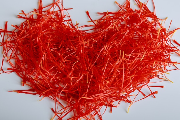 Fili di zafferano a forma di cuore su uno sfondo bianco. Preparazione di fili di zafferano per l'essiccazione prima dell'uso in cucina, cosmetologia o medicina.