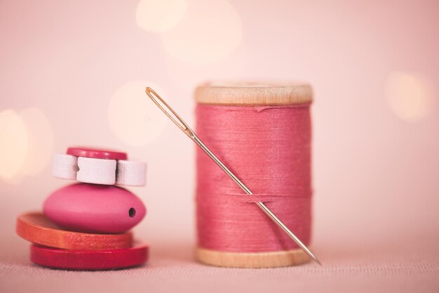 Filo di cotone rosa sul cucchiaio con pila di bottoni da vicino. Messa a fuoco selettiva.