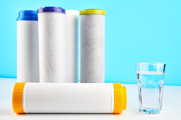 Filtri per l'acqua. Cartucce di carbone e un bicchiere su sfondo bianco blu. Sistema di filtraggio domestico.
