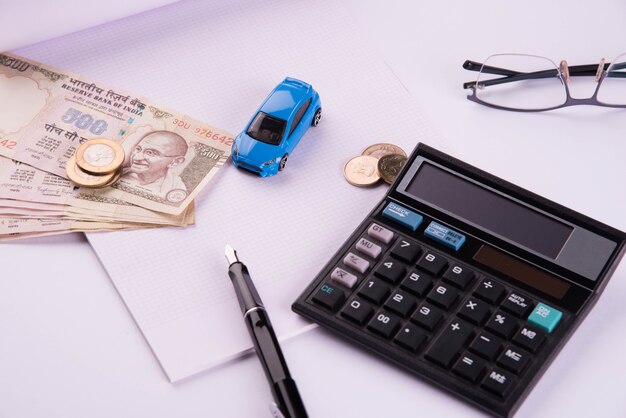 Finanziamento automatico o prestito in India - Concetto che mostra il modello di auto giocattolo, chiavi, banconote in valuta indiana e calcolatrice per calcoli EMI ecc. disposti su sfondo chiaro