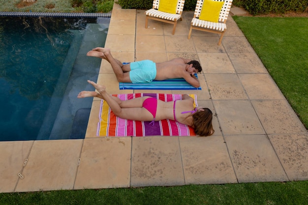 Fine settimana a casa insieme. Veduta dall'alto di una coppia caucasica che indossa abiti da spiaggia in un giardino, sdraiata accanto a un bagno che prende il sole