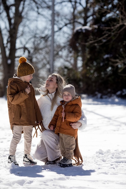 Fine settimana invernale Madre e due figli in vestiti invernali caldi che si divertono a camminare nella foresta invernale tra gli alberi