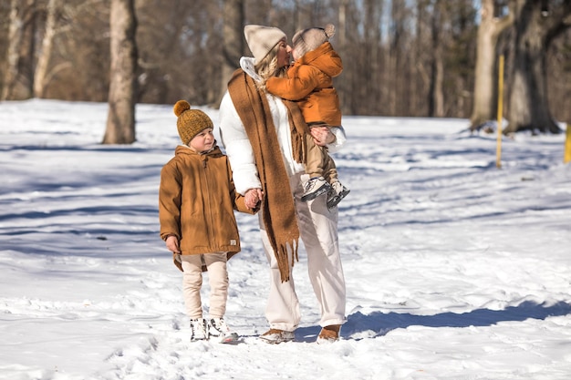 Fine settimana invernale Madre e due figli in vestiti invernali caldi che si divertono a camminare nella foresta invernale tra gli alberi