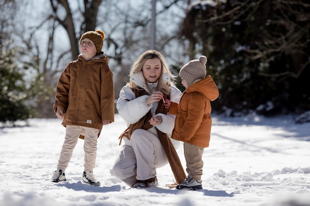 Fine settimana invernale Madre e due figli in vestiti invernali caldi che si divertono a camminare nella foresta invernale tra gli alberi