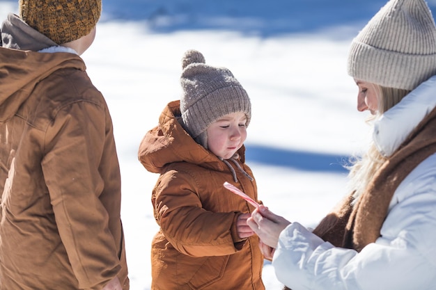 Fine settimana invernale Madre e due figli in vestiti invernali caldi che si divertono a camminare nella foresta invernale tra gli alberi