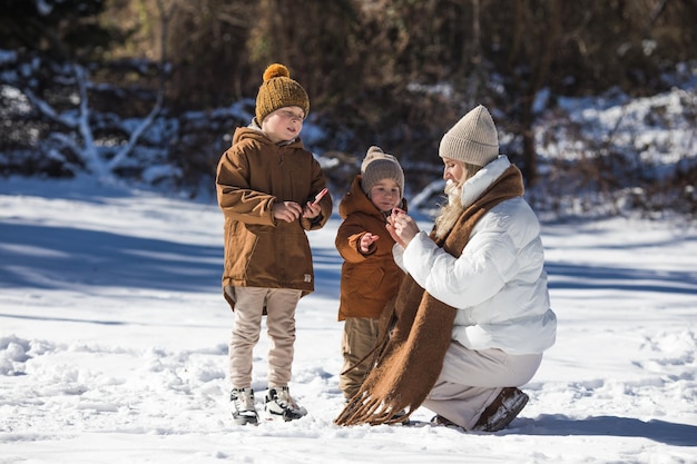 Fine settimana invernale Madre e due figli in vestiti invernali caldi che si divertono a camminare nella foresta invernale tra gli alberi