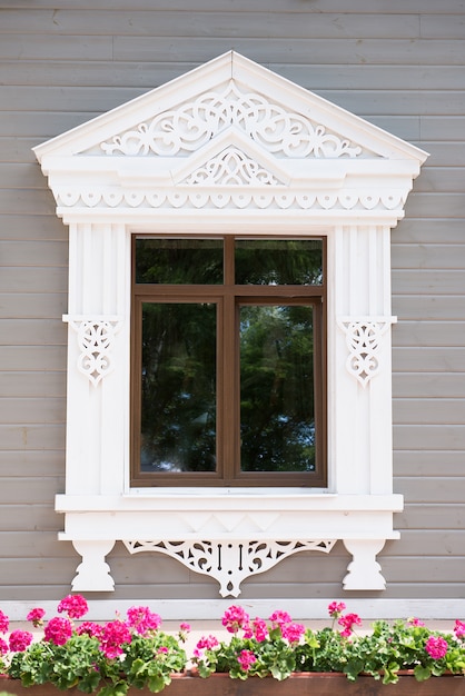 Finestra bianca ornata con la casa di legno dei fiori rossi