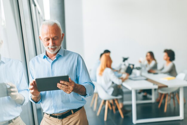 Finestra facente una pausa dell&#39;uomo d&#39;affari senior con la compressa digitale in sua mano