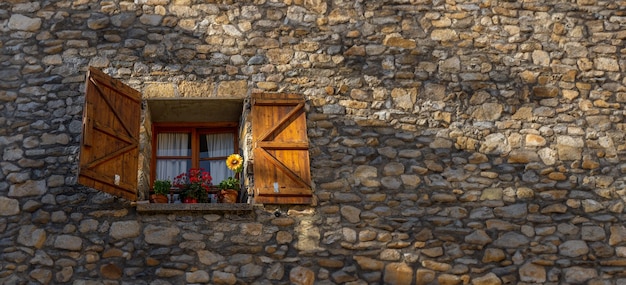 Finestra in legno con le persiane aperte di una vecchia casa rurale in pietra nei Pirenei e vasi di fiori