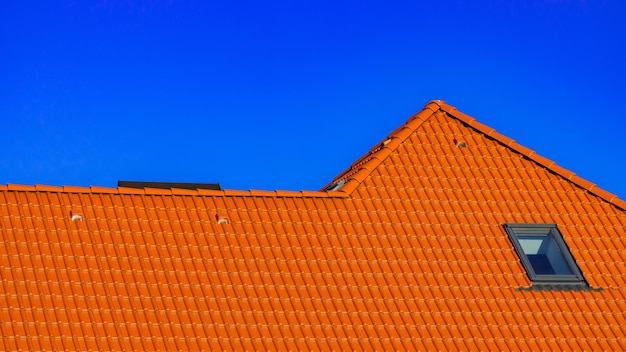 Finestra sul tetto della casa con tegole arancioni su uno sfondo di cielo blu primaverile Foto di alta qualità