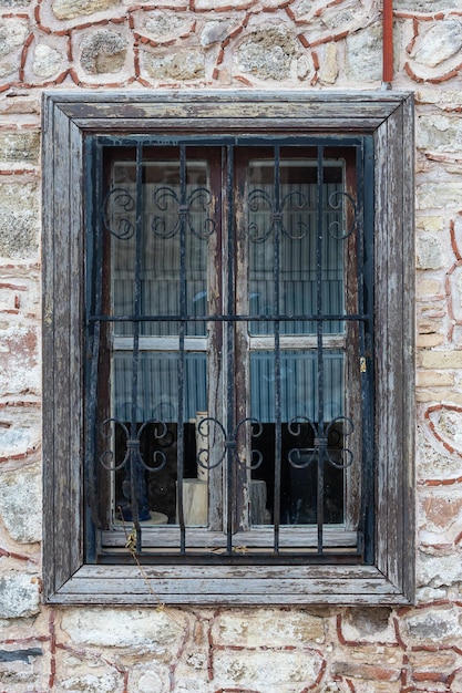 Finestra vintage in legno marrone del primo piano dietro le sbarre in una vecchia casa di pietra