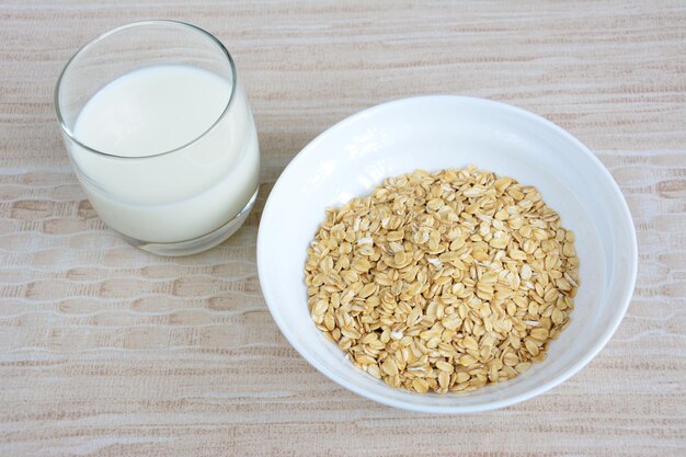 fiocchi d'avena in una ciotola bianca isolata con un bicchiere di latte su sfondo beige, primo piano