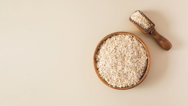 Fiocchi d'avena in una ciotola di legno su fondo beige Mangiare sano