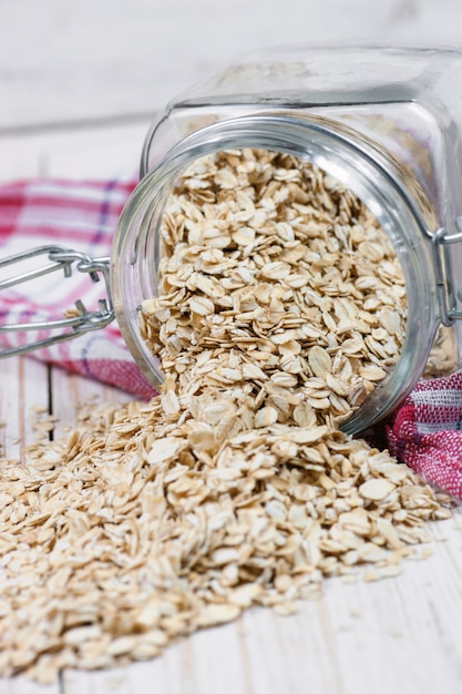 Fiocchi di avena che si rovesciano dal barattolo di vetro.