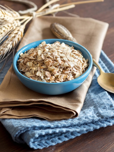 Fiocchi di avena crudi in una ciotola su un tovagliolo su una fine di legno della tavola su