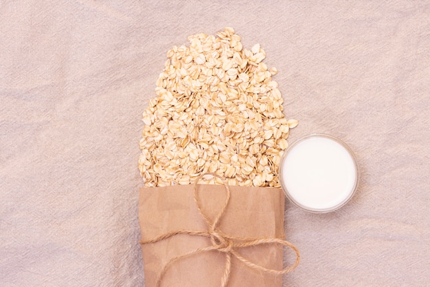 Fiocchi di avena naturali secchi. Farina d'avena da un sacchetto di carta ecologico. Sfondo di lino naturale con eco bag e fiocchi d'avena. Una tazza di latte