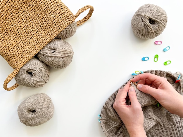 Fiocchi di filati di lana nel cesto fatto a mano marcatori per la maglieria e mani di donne a maglieria pullover