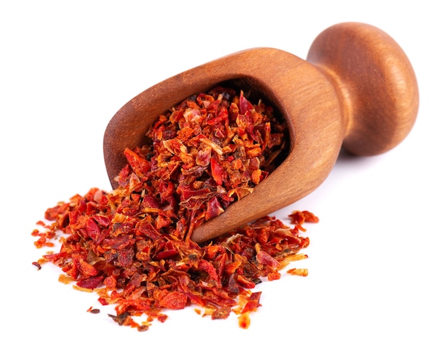 Fiocchi di paprika rossa essiccata in paletta di legno isolata su sfondo bianco Spezie ed erbe aromatiche