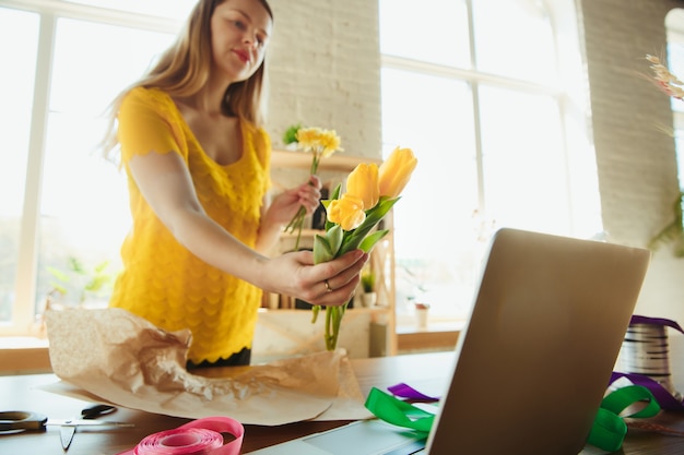 Fioraio al lavoro: la donna mostra come realizzare un bouquet con i tulipani. La giovane donna caucasica offre un seminario online per fare regali, regalo per la celebrazione. Lavorare a casa mentre è isolato, in quarantena concetto.