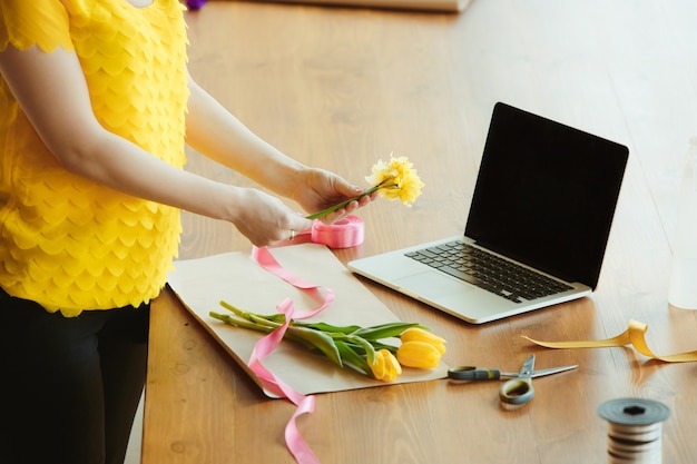 Fioraio al lavoro: la donna mostra come realizzare un bouquet con i tulipani. La giovane donna caucasica offre un seminario online per fare regali, regalo per la celebrazione. Lavorare a casa mentre è isolato, in quarantena concetto.