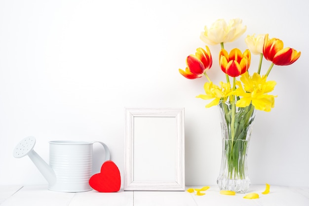 Fiore del tulipano in vaso di vetro con il posto della cornice immagine sul fondo della tavola in legno bianco contro il muro pulito a casa, primi piani, concetto di arredamento festa della mamma