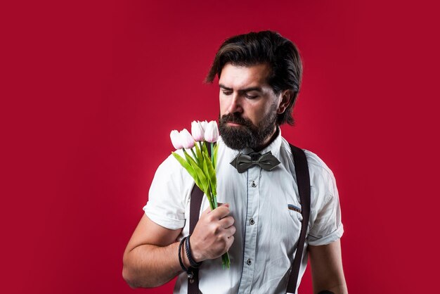 Fiore di primavera presente uomo romantico in bretelle e papillon uomo fiducioso ed elegante tenere fiori di tulipano regalo per data d'amore vecchio stile hipster barbuto con bouquet
