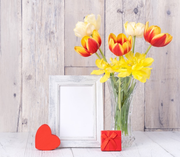 Fiore di tulipano in vaso di vetro con decorazione cornice su tavolo in legno parete di fondo a casa, primo piano, concetto di design per la festa della mamma.