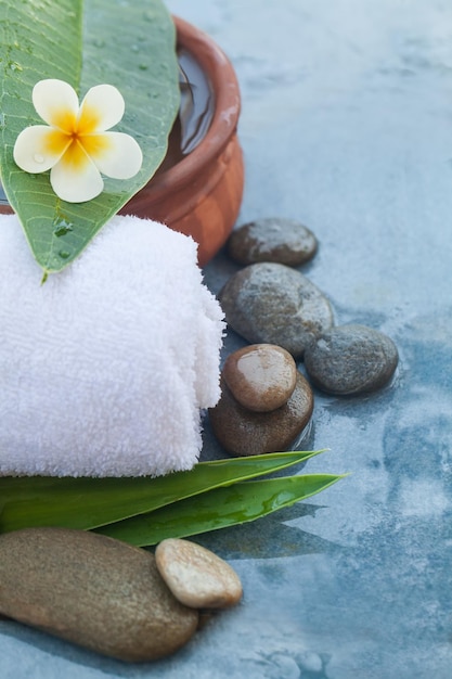 Fiore tropicale e asciugamano e pietre con luce solare per il trattamento di massaggio su sfondo blu