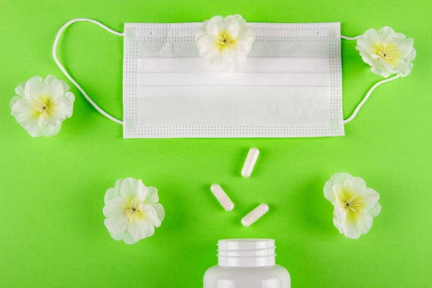 fiori bianchi maschera medica e flacone di capsule pillole su sfondo verde