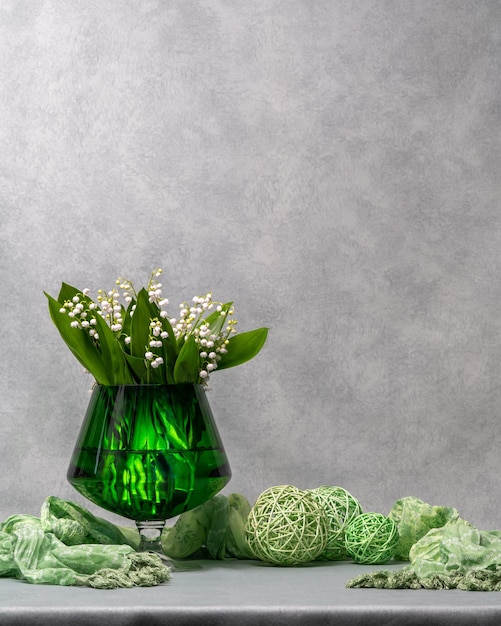 Fiori bianchi mughetti in un vaso trasparente verde accanto a una sciarpa verde tre palle