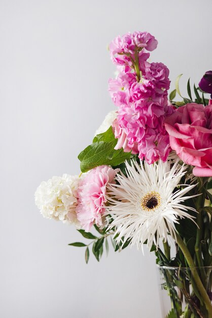 Fiori bianchi rosa e pastello in vaso di vetro moderno sulla fine verticale del fondo della parete grigia