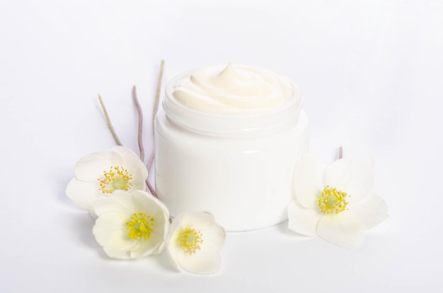 Fiori carini e un vasetto di crema per il corpo naturale isolato su sfondo bianco