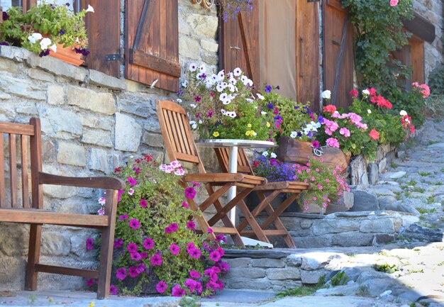 Fiori colorati in vaso e sedie di fronte alla facciata di una casa alpina in un villaggio