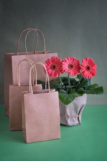 Fiori della margherita della gerbera di corallo e sacchetti della spesa del papper del mestiere sul fondo del Libro Verde, copia-spazio