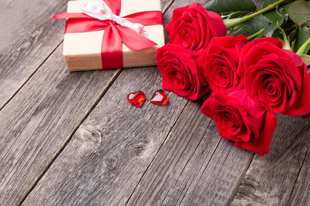 Fiori delle rose rosse e contenitore di regalo sulla tavola di legno grigia