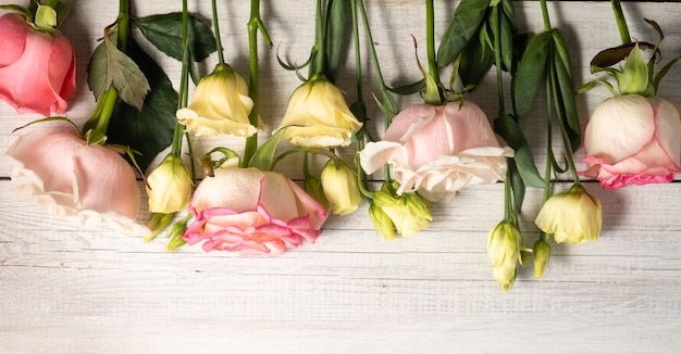 fiori di eustoma e rose rosa su superficie di legno in stile vintage.