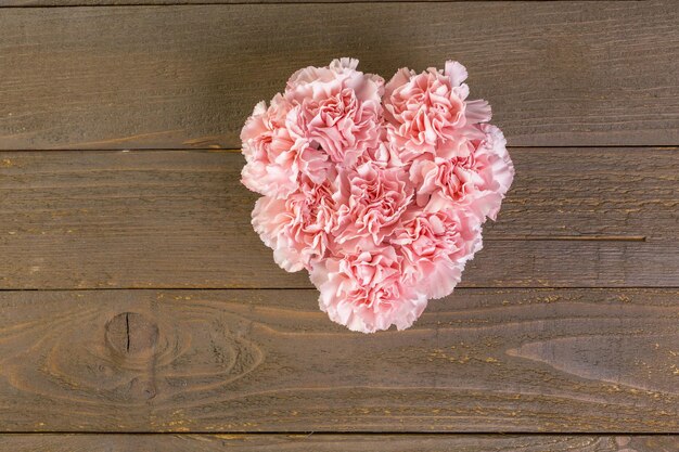 Fiori di garofani in disposizione a forma di cuore su tavola di legno.