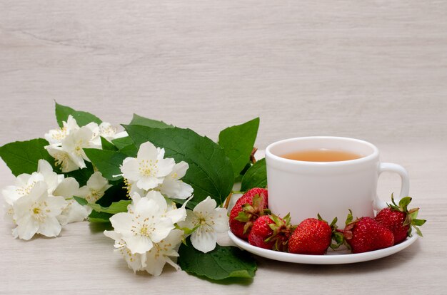 Fiori di gelsomino, tazza bianca con tè, fragole, primo piano