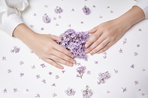 Fiori di giglio di primavera nelle mani di una donna sdraiata su un tavolo bianco. Cosmetici naturali per le mani, mani antirughe. Bellezza naturale di una donna