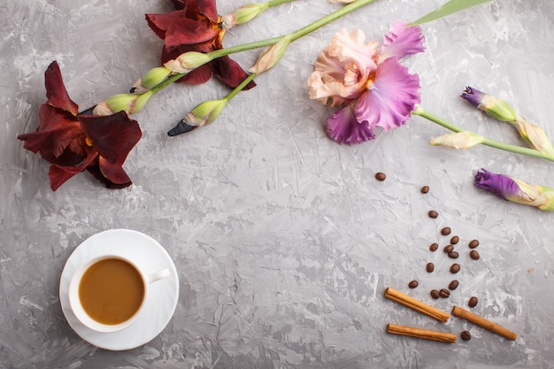 Fiori di iris viola e bordeaux e una tazza di caffè sul cemento grigio